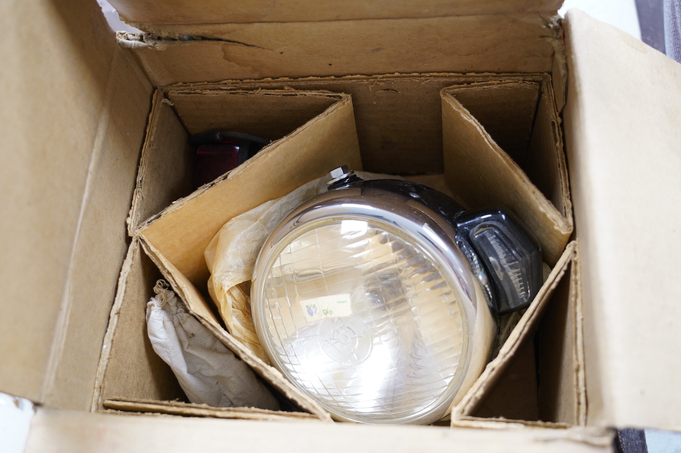 A boxed and apparently unused Lucas 575 motorcycle headlamp, in its original card box with the inner card packing pieces. Condition - fair to good, fading and wear to the box